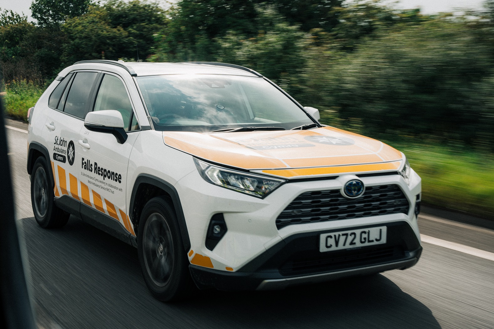 A white St John Ambulance falls response vehicle driving along a road. The vehicle emblazoned with the charity's name and maltese cross logo