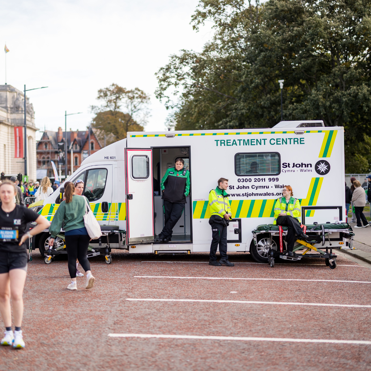 Mobile treatment centre vehicle at the Cardiff Half Marathon. Printed on the side of the vehicle, there is the St John Ambulance Cymru logo, phone number and website. Three volunteers in uniform are talking in front of the vehicle.